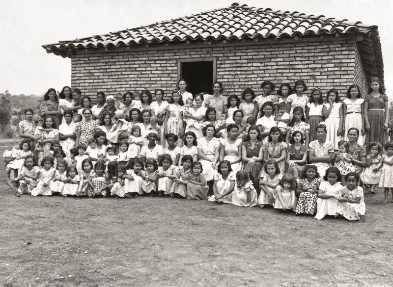 Dezenas de pessoas posando em frente à casa de telhado de barro que abrigou a casa em Ceres.