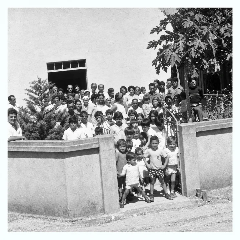 Adultos e muitas crianças sentados sobre o muro e reunidos em frente à sede antiga.