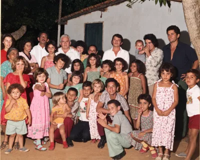 Famílias reunidas em frente a uma casa, adultos e muitas crianças posando ao sol.