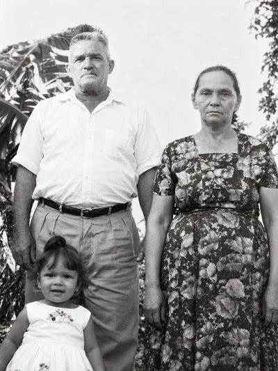 Zé Paulista e Dona Chiquinha com uma criança pequena entre eles, diante de bananeiras.