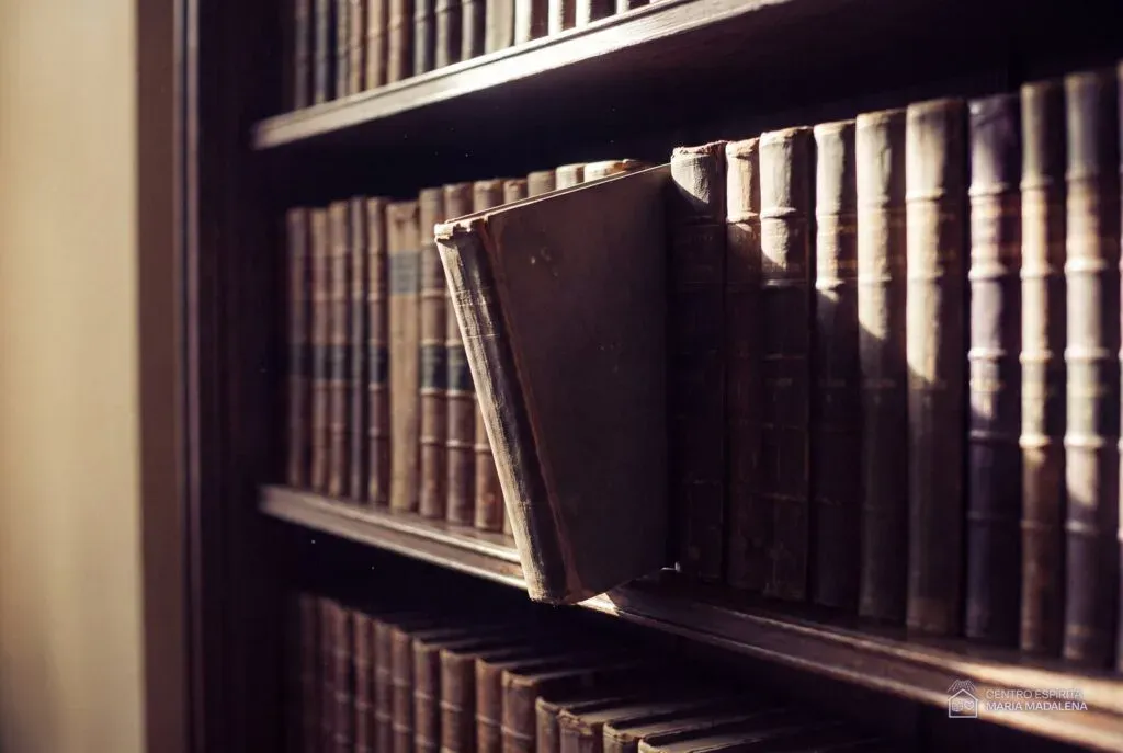 Estante de livros antigos com um único volume puxado à frente, iluminado por um feixe de luz