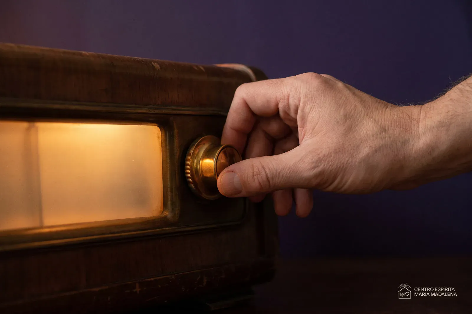 Uma mão girando devagar o botão de sintonia de um rádio antigo de madeira